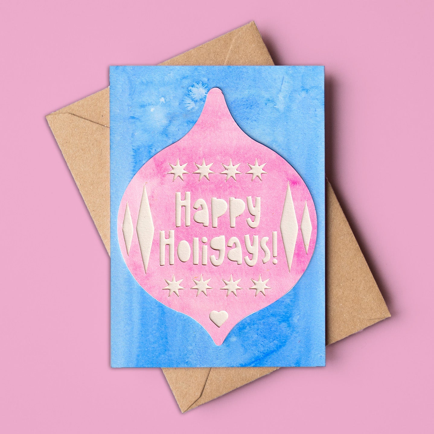 A6 Christmas card with a large pink bauble design on a blue watercolour background, featuring the text “Happy Holigays!” in cream. Includes kraft envelope. Made in Australia, wholesale available.