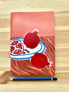 A5 lined notebook featuring a still life of pomegranates on a plate done in linoprint style, stationery made in Australia, available for wholesale