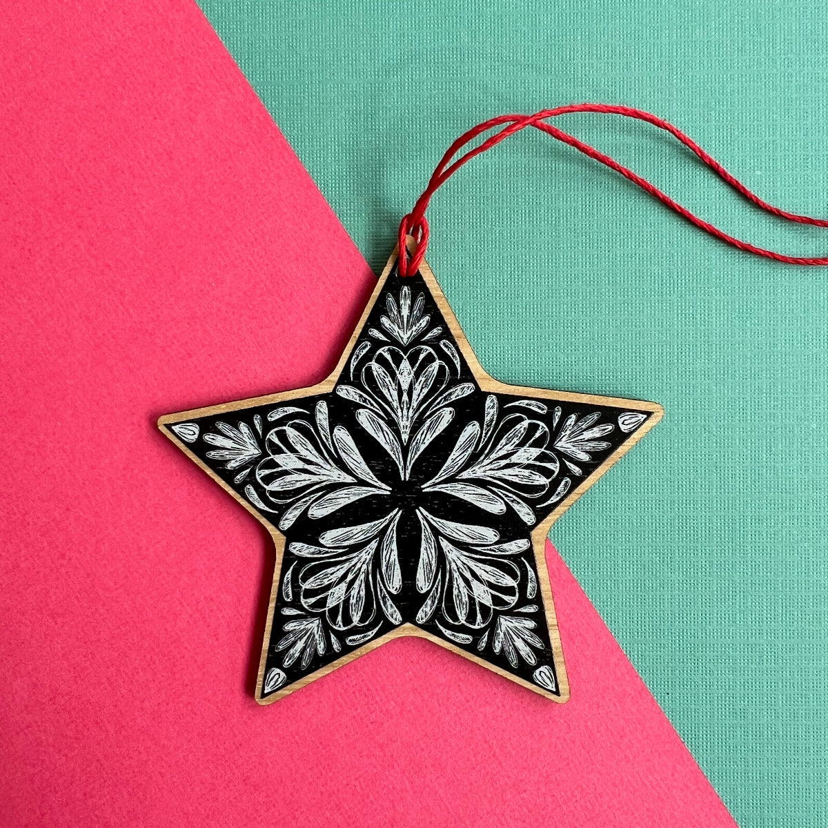 A star-shaped Christmas ornament with a black and white floral pattern, made of wood, and hanging from a red cord. Made from sustainable Eucalyptus in Australia. 