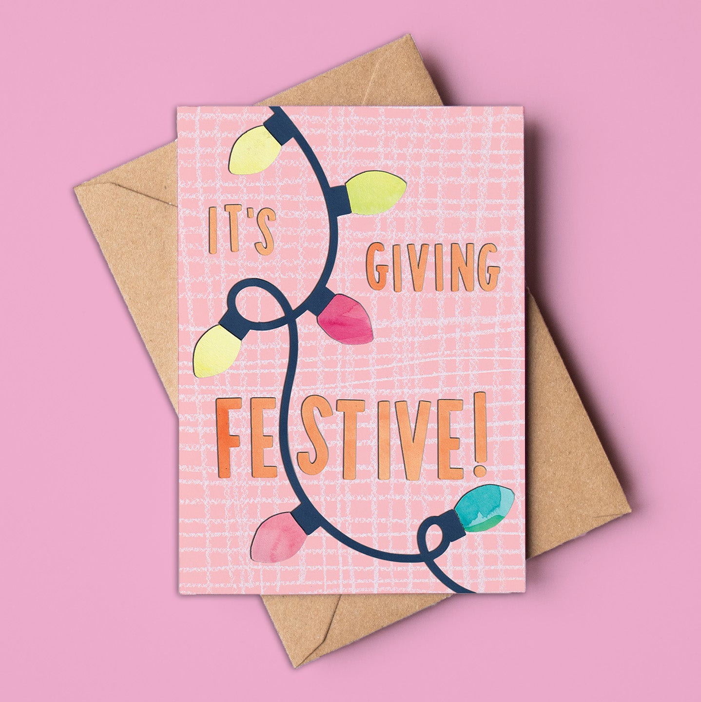 A6 pink Christmas card featuring the phrase “It’s Giving Festive!” with colourful fairy lights, kraft envelope included. Non-traditional holiday design, made in Australia, wholesale available.
