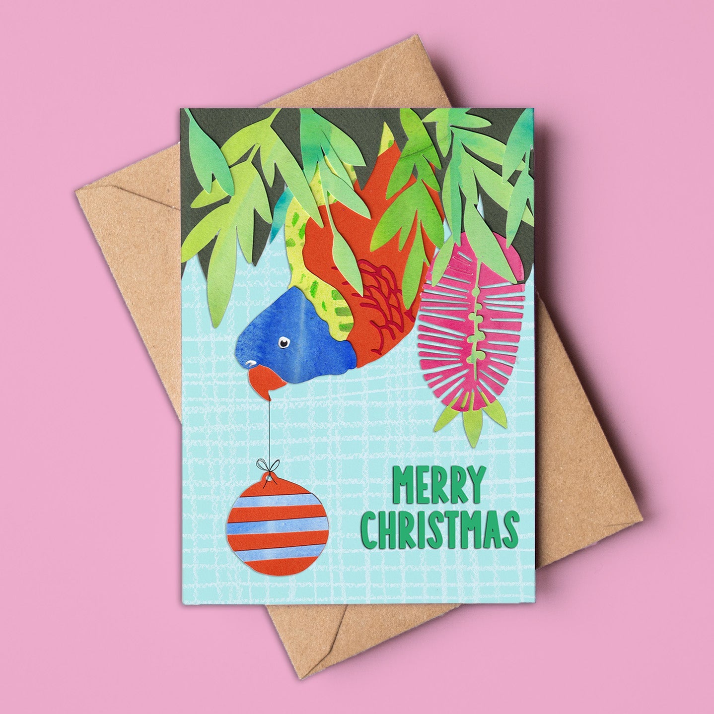 A6 Christmas card showing a colourful rainbow lorikeet hanging upside down from tropical greenery, next to a striped bauble and “Merry Christmas” text. Includes kraft envelope. Made in Australia, wholesale available.