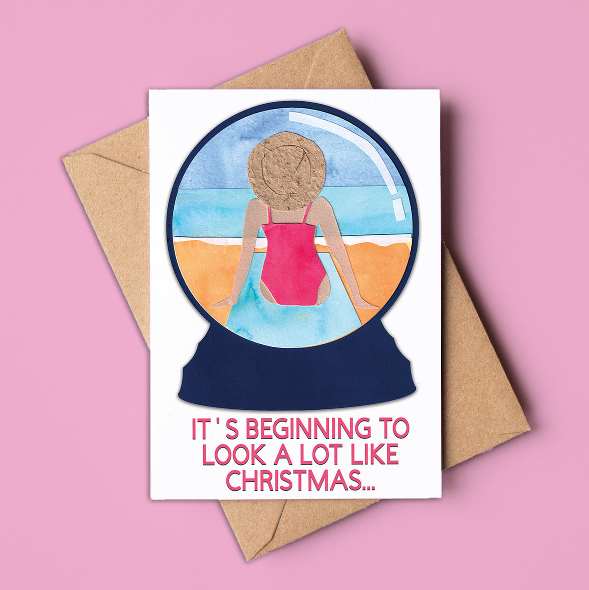 Card with a snowglobe illustration of a person in a swimsuit and text &#39;It&#39;s beginning to look a lot like Christmas&#39; on a pink background. Made in Australia and available for wholesale.