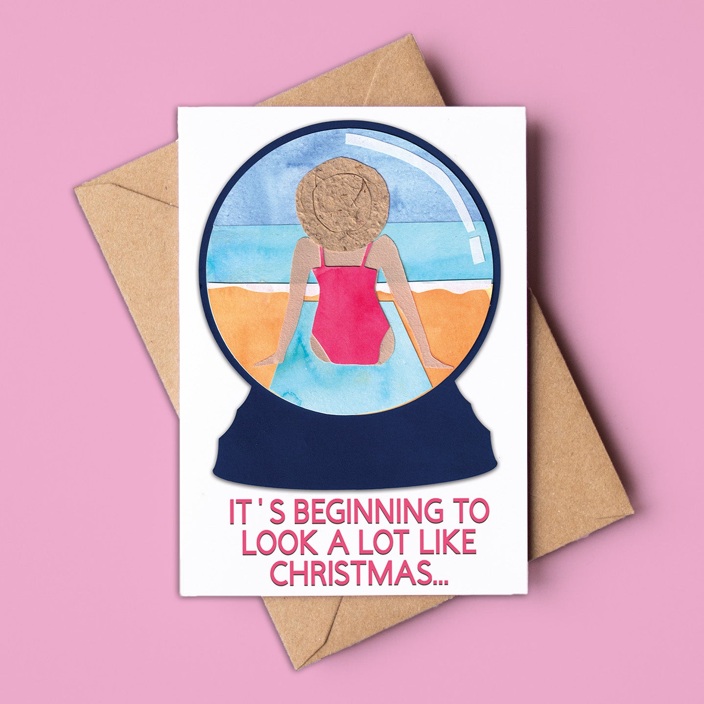 Card with a snowglobe illustration of a person in a swimsuit and text 'It's beginning to look a lot like Christmas' on a pink background. Made in Australia and available for wholesale.