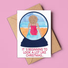 Card with a snowglobe illustration of a person in a swimsuit and text 'It's beginning to look a lot like Christmas' on a pink background. Made in Australia and available for wholesale.