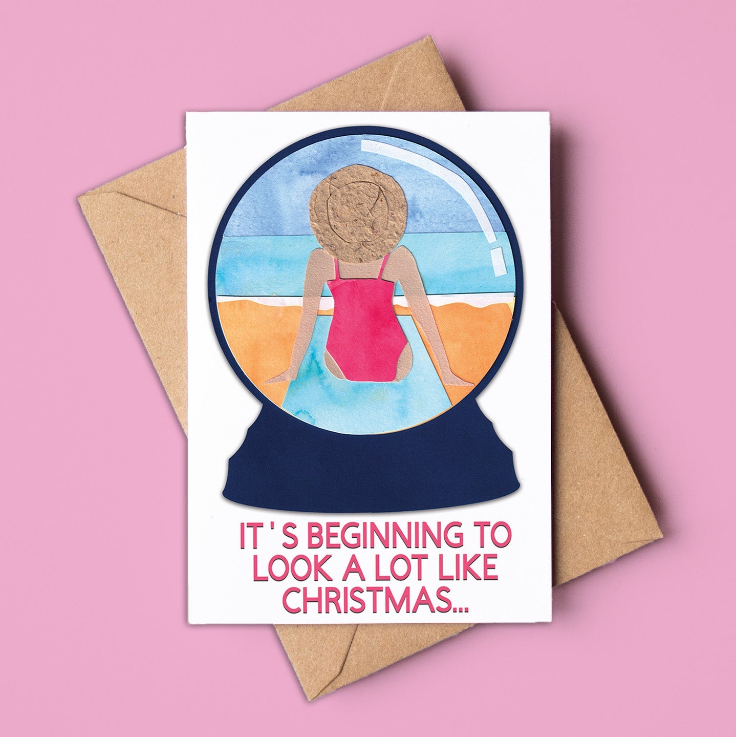 Card with a snowglobe illustration of a person in a swimsuit and text 'It's beginning to look a lot like Christmas' on a pink background. Made in Australia and available for wholesale.